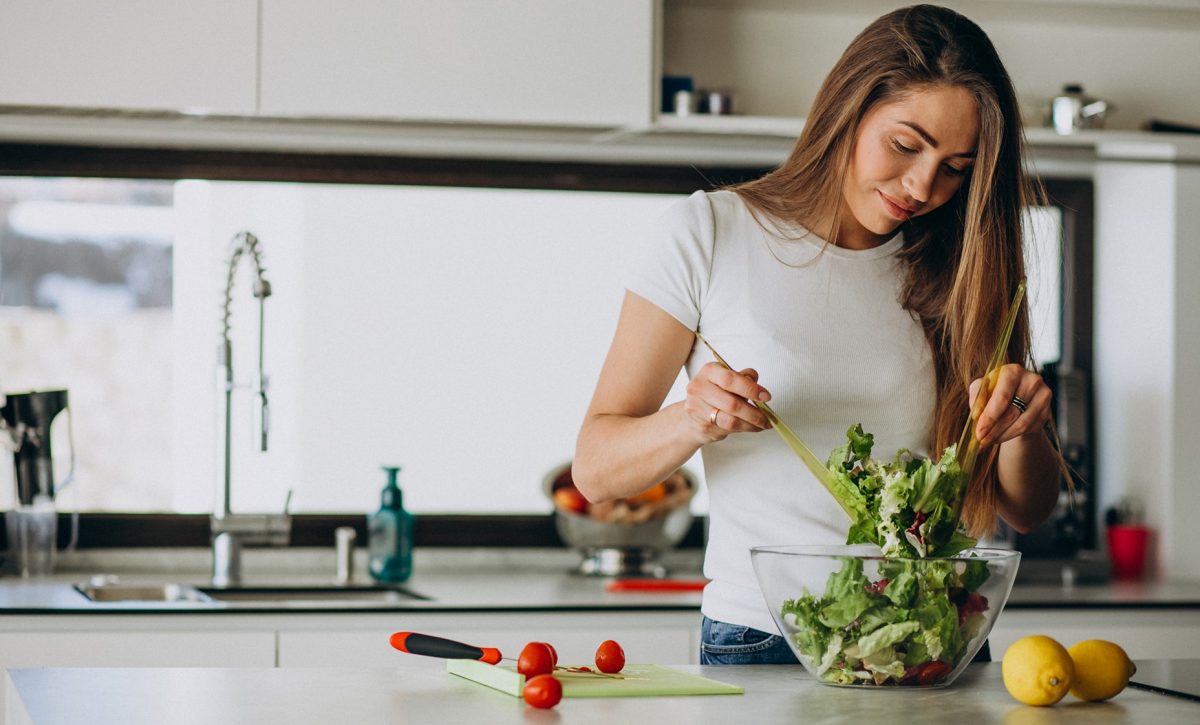 Young woman making salad at the kitchen