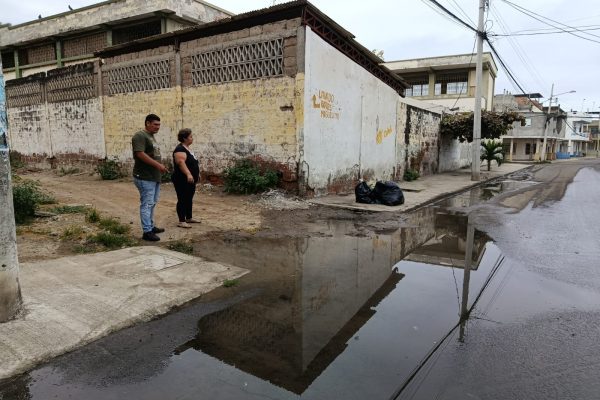 Rita González junto a otro vecino mostrando una de las filtraciones de agua en la esquina de la ex escuela Abraham Linconl donde se evidencian dos fugas de agua potable en la acera.