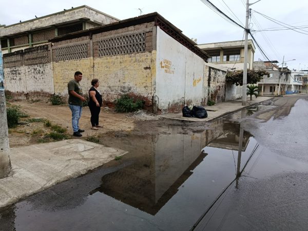 Rita González junto a otro vecino mostrando una de las filtraciones de agua en la esquina de la ex escuela Abraham Linconl donde se evidencian dos fugas de agua potable en la acera.